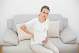 Suffering pregnant woman looking seriously at camera touching her injured back
