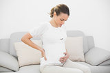 Worried pregnant woman touching her injured back sitting on couch