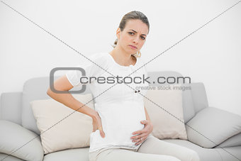 Beautiful pregnant woman looking seriously at camera holding her injured back