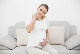 Attractive pregnant woman holding her injured neck while touching her belly