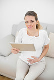 Pregnant woman holding her tablet smiling at camera