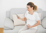 Cute pregnant woman touching her belly while using her tablet