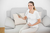 Content pregnant woman holding her tablet smiling at camera