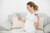 Cute cheering pregnant woman using her tablet for home shopping