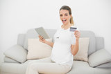 Cheering pregnant woman showing her tablet and credit card looking at camera