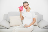 Happy pregnant woman shaking a pink piggy bank