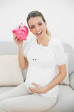 Beautiful pregnant woman shaking a piggy bank while holding her belly