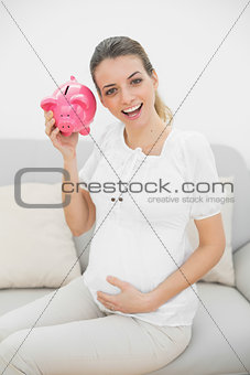 Beautiful pregnant woman shaking a piggy bank while holding her belly