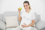 Beautiful smiling pregnant woman showing a green apple holding her belly