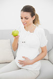 Smiling pregnant woman looking at  green apple holding it