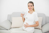 Peaceful pregnant woman holding a glass of water touching her belly