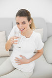 Attractive pregnant woman touching her belly holding a glass of water
