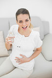 Happy pregnant woman holding a glass of water smiling at camera