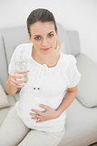 Cute pregnant woman holding a glass of water looking seriously at camera