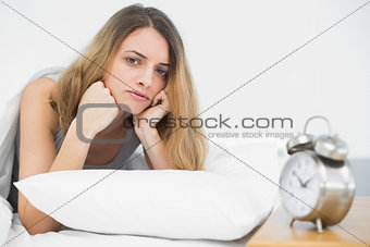Serious brunette woman lying on her bed under the cover