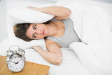 Exhausted brunette woman covering her ears with pillows