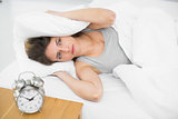 Annoyed woman covering her ears with pillows