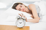 Lovely woman turning off the alarm clock with eyes closed