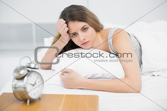 Serious young woman lying on her bed under the cover