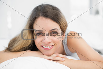 Beautiful brunette woman smiling at camera lying on her bed