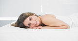 Attractive brunette woman smiling cheerfully at camera lying on her bed