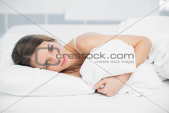 Attractive calm woman lying on her bed holding her cover