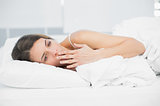 Beautiful yawning woman lying under the cover on her bed