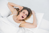 Young yawning woman lying on her bed in bedroom