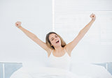 Brunette woman yawning while stretching out sitting on her bed