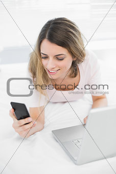 Content young woman using her smartphone lying on her bed