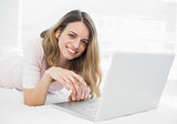 Smiling young woman lying in front of her laptop