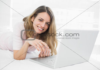 Smiling young woman lying in front of her laptop