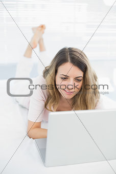 Cute young woman using her notebook lying on her bed