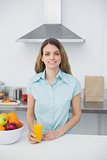 Content young woman posing in kitchen holding a glass of orange juice