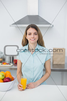 Content young woman posing in kitchen holding a glass of orange juice