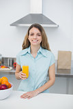Beautiful brunette woman posing standing in kitchen holding a glass of orange juice