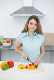Cute young woman cutting vegetables standing in kitchen