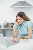 Content young woman working with her laptop standing in her kitchen