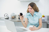 Content brunette woman making use of her smartphone holding a cup