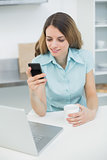 Cute brunette woman holding her smartphone and a cup
