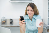 Beautiful young woman using her smartphone holding a cup