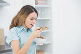 Lovely woman eating cereals while standing in her kitchen