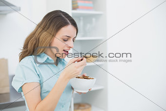 Lovely woman eating cereals while standing in her kitchen