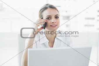 Softly smiling businesswoman sitting at her desk while phoning
