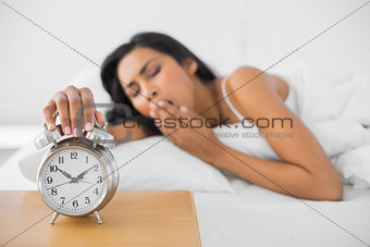 Lovely yawning woman turning off the retro alarm clock