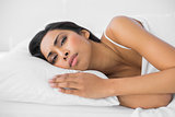 Young attractive woman lying on her bed wrinkling her brow