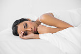 Thoughtful dark haired woman lying under the cover on her bed