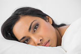 Attractive woman lying in her bed looking seriously at camera
