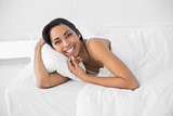 Gorgeous smiling woman lying under the cover on her bed