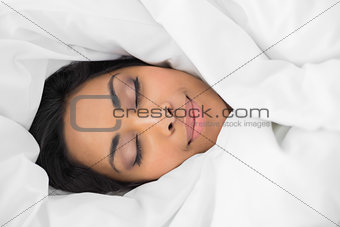 Lovely smiling woman lying on bed under cover